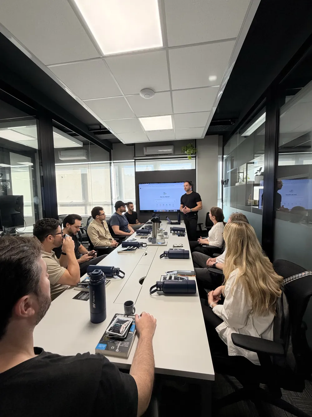 Treinamento da Marvee com participantes ao redor da mesa e apresentação do Hub na tela.